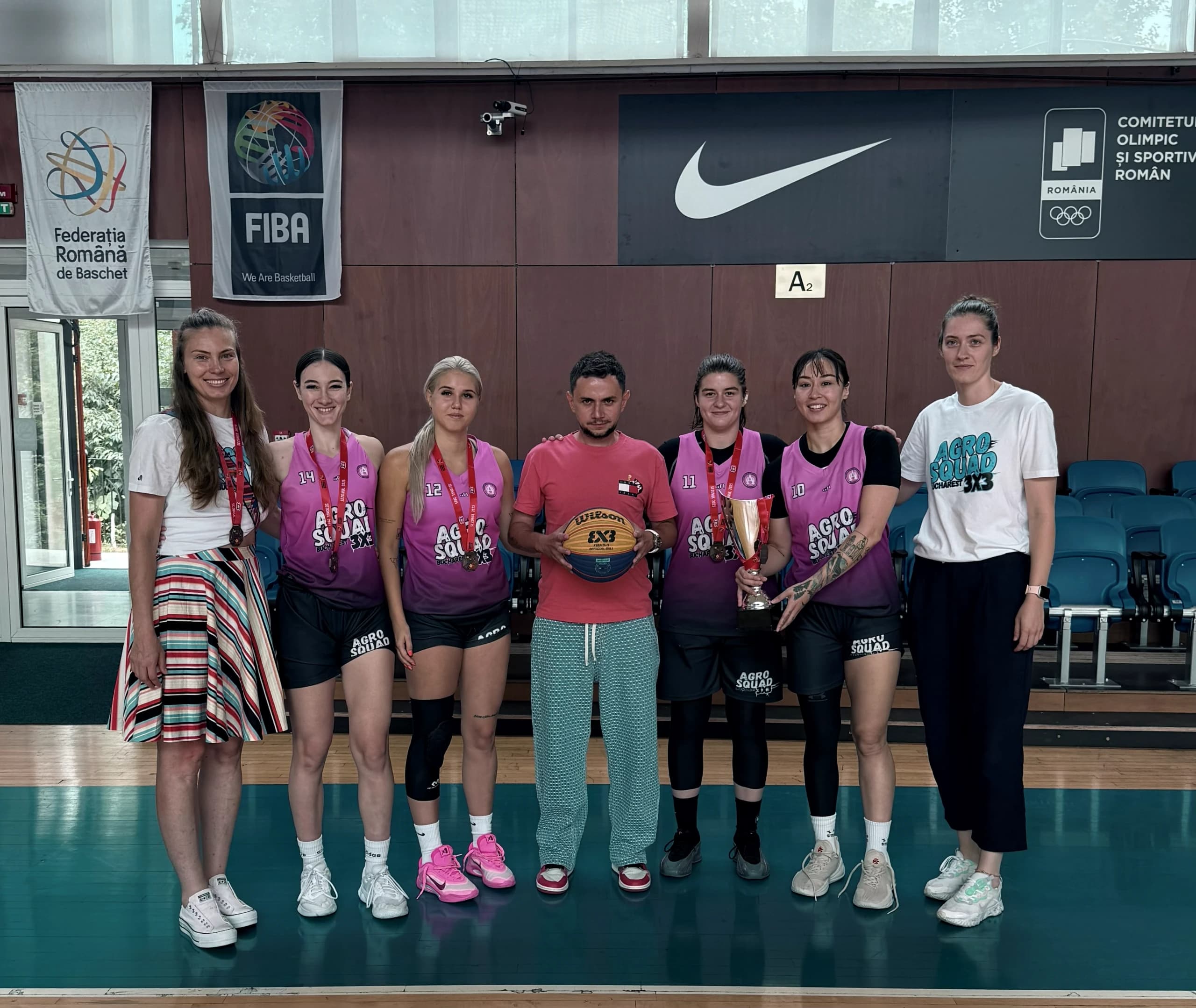 Echipa feminină de 3x3 și staful, cu trofeul și mingea, sub bannerele competiției