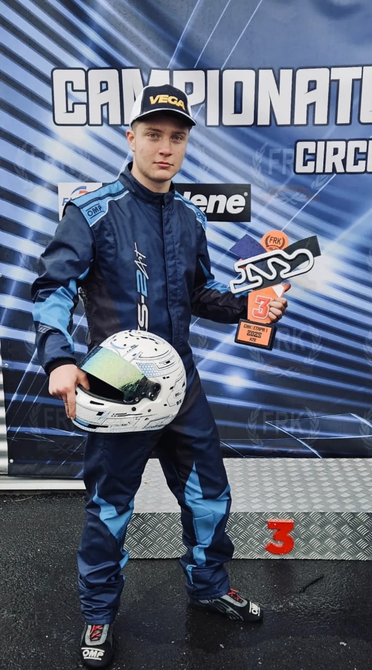 Pilotul cu trofeul și casca în mână, pe treapta a treia a podiumului