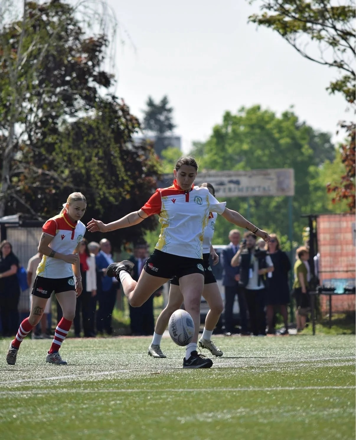 Jucătoare de rugby lovind mingea cu piciorul, cu publicul în spate