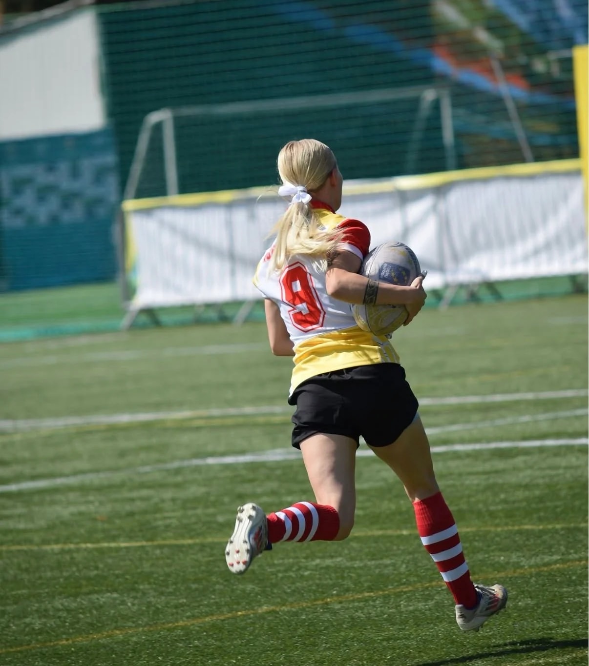 Jucătoarea cu numărul 9 aleargă cu mingea de rugby pe un culoar liber