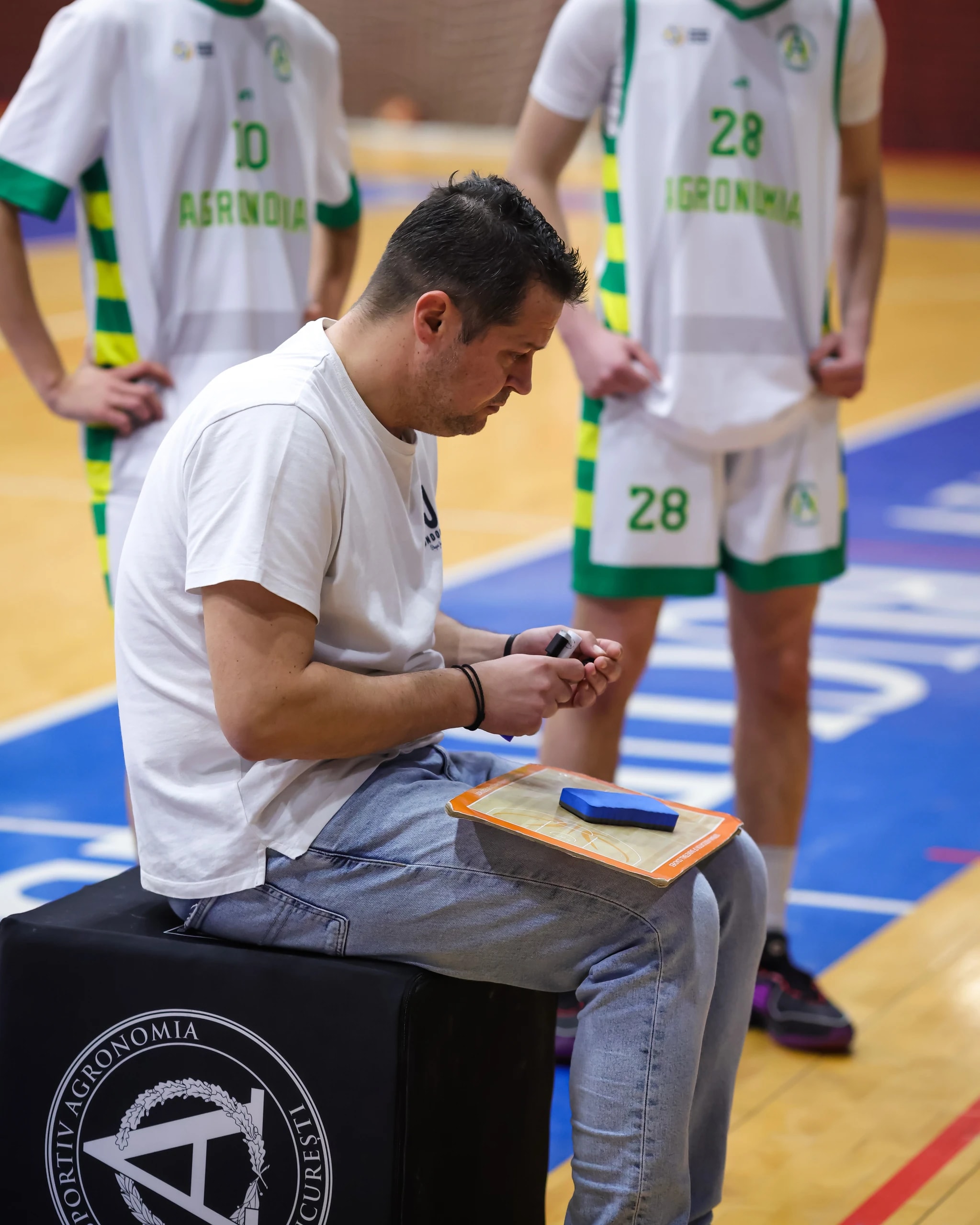 Antrenorul cu tabla de tactică, pe banca echipei de baschet